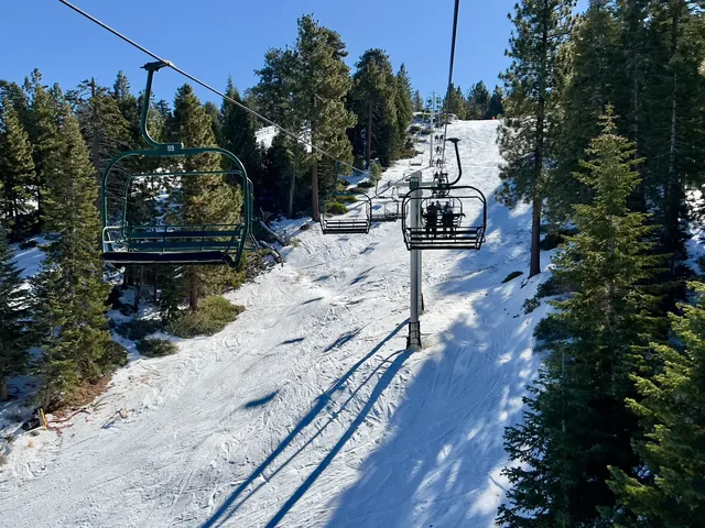 Rear view of unidentified skiers and snowboarders on chairlift going up snow covered mountain at Big Bear California