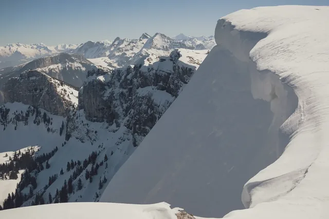 Massive Snow Cornice Overlooking Rocky Cliffs and Distant Mont Blanc Range Near Geneva, French-Swiss Alps